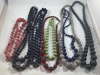 Top-down view showing all 9 assorted vintage bead necklaces in various colors and bead sizes.