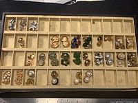 Shows the complete collection of various vintage costume jewelry earrings arranged in a compartment organizer tray with a ruler beneath for size reference. Includes styles in silver tone, gold tone, faux pearl, and glass stone accents in multiple colors.