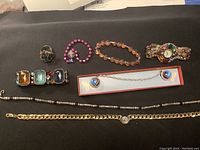 Photo showing assortment of vintage costume jewelry pieces on dark background including necklaces, bracelets, rings, and a decorative watch.