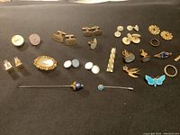 Full lot of vintage costume jewelry including cuff links, pins, brooches, tie clips, and rings on black background