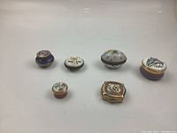 Top view of all six miniature pill boxes in a row showing various colors and floral patterns.