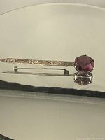View of vintage sterling silver pin with engraved detailing and large round purple glass stone in prong setting, showing the front and side details.