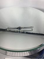 Art Deco sterling silver pin with a blue sapphire set in the center, shown on reflective round mirror surface.