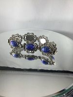 Front and side views of a vintage silver bracelet with blue stones on a reflective surface.