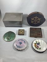 Full view of assorted vintage compact cases, jewelry case, and pill box arranged on white background.