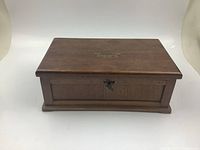 Front view of closed vintage wooden keepsake box with metal lock and brass emblem.