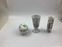 Four floral ceramic decor pieces: round trinket box, footed vase, tall slender vase