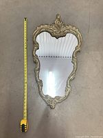 Full view of vintage ornate wall mirror with measuring tape to show height approximately 21 inches.