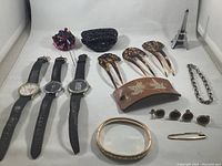 Vintage watches, tortoiseshell hair combs, hair barrette, safety pin, chain bracelet, and clip-on earrings on white surface.