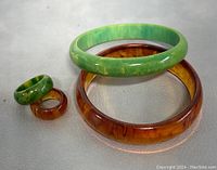 Photo showing both green and amber bakelite bangles and matching rings with marbled and swirl patterns on a light background.