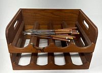 Photo shows two stacked Mid-Century Modern teak wine racks with eleven vintage Japanese fondue forks placed on top, each fork has a wooden handle with colored tips.