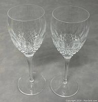 Two Waterford Monique Lhuillier Ellipse wine glasses on neutral background from the front showing detailed diamond and oval cut pattern and long stems.
