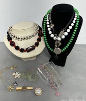 Multiple jewelry pieces displayed including bead necklaces, spike necklace, pendants, and earrings on necklace busts and lying on tabletop.