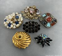 Six brooches including the signed Miracle Scottish brooch with multiple stones and five assorted costume brooches.