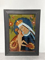 Full view of framed reverse glass painting showing Virgen Mary and Christ Child with floral designs on green background.