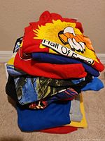 Stack of assorted men's t-shirts and tank tops showing varying colors and patterns including graphic designs.
