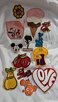 Photo showing 14 different vintage unused iron-on patches laid out on white fabric background.