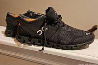 Side angle view of the pair of black On Cloud running trainers showing details of knit upper, outsole design, and branding.