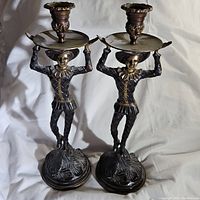 Pair of bronze Harlekin candlesticks standing side by side on a white cloth background, showing overall appearance and size.