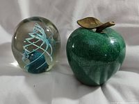 Both paperweights side by side on white fabric background. Shows size comparison and materials.