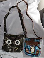 Pair of vintage owl-themed shoulder bags, one camo with floral owl eyes and butterfly patch, the other blue with owl patch and brown trim.