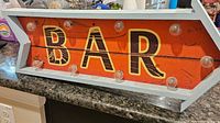 Full frontal view of the bar sign showcasing the orange wooden planks with decorative 'BAR' text and surrounding clear light bulbs, placed on a countertop.