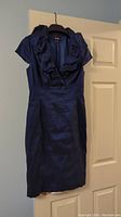 Full front view of navy blue Adrianna Papell cocktail dress on hanger showing ruffled collar, cap sleeves, and fitted silhouette.