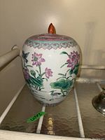 Front view of the lidded pottery vase showing pink lotus flowers and bird design on white glaze.
