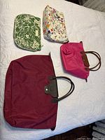 Four assorted bags and purses arranged on white bedspread showing varying sizes and colors
