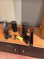Photo showing assorted camera equipment including lens cases, flash units, timers, and small tripod on wooden surface.