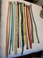 Full view of 12 assorted women's belts laid side-by-side showing colors, buckle styles and materials.