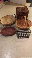 Five various baskets arranged on floor showing different materials and shapes.