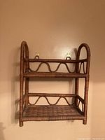 Two-tier rattan shelving unit with decorative weaving and loops, mounted on plain wall.