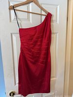 Front view of red satin one-shoulder dress on hanger, showing single thin black strap and pleated detail.