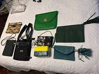 Top view of eight assorted purses, clutches, a wallet and an iPad/tablet sleeve laid out on white surface.