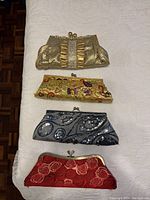 Four evening clutches arranged flat on white quilted surface showing details of fabric, sequins, rhinestones and hardware