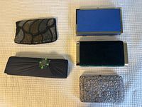 Five evening clutches displayed on a textured white surface, showing details and variety in design.