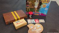 Full view of the lot showing wooden case with dominoes, box of dominoes, Yahtzee dice shaker, playing cards, cribbage board, and Kid-in-a-Bubble game box.