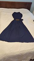 Full view of navy blue chiffon dress laid flat on bed showing length and belt detail.