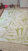 Large green and white rectangular patio rug with botanical leaf pattern spread on the floor.