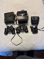 Three binoculars laid out side by side with their black carrying cases visible, showing relative size and form.