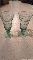 Pair of crystal green Adirondack pattern glasses each about 7 inches tall and 4 inches wide, showing the front and side views with detailed pattern and bulbous stem design.