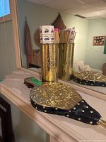 Fireplace bellows with brass embossed front and black leather, alongside brass match holder with matches and matchbox.