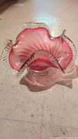 Side view of vintage glass bowl with cranberry center and clear ruffled, swirled edges on pedestal base.