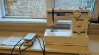 Photo of Vintage Domestic sewing machine next to window with foot pedal and original manual laying beside it on the table.
