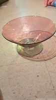 Side angle showing pink translucent conical glass bowl with green pedestal base on a tiled floor.