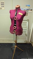 Front view of pink fabric-covered dress form on wooden tripod stand showing front dials and top neckline.