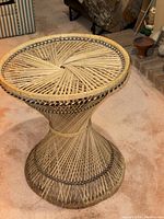 Side view of the wicker round side table on a carpeted floor, showing the woven wicker design and shape.