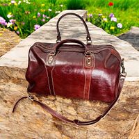 Front-quarter view of burgundy leather weekender bag on stone surface