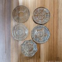All five heavy cut glass round platters arranged on wood floor to show size and relative patterns